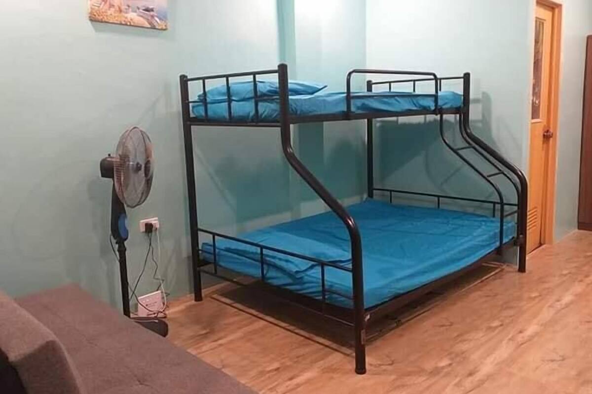 A bunk bed with a blue mattress, a standing fan, and a wooden floor.