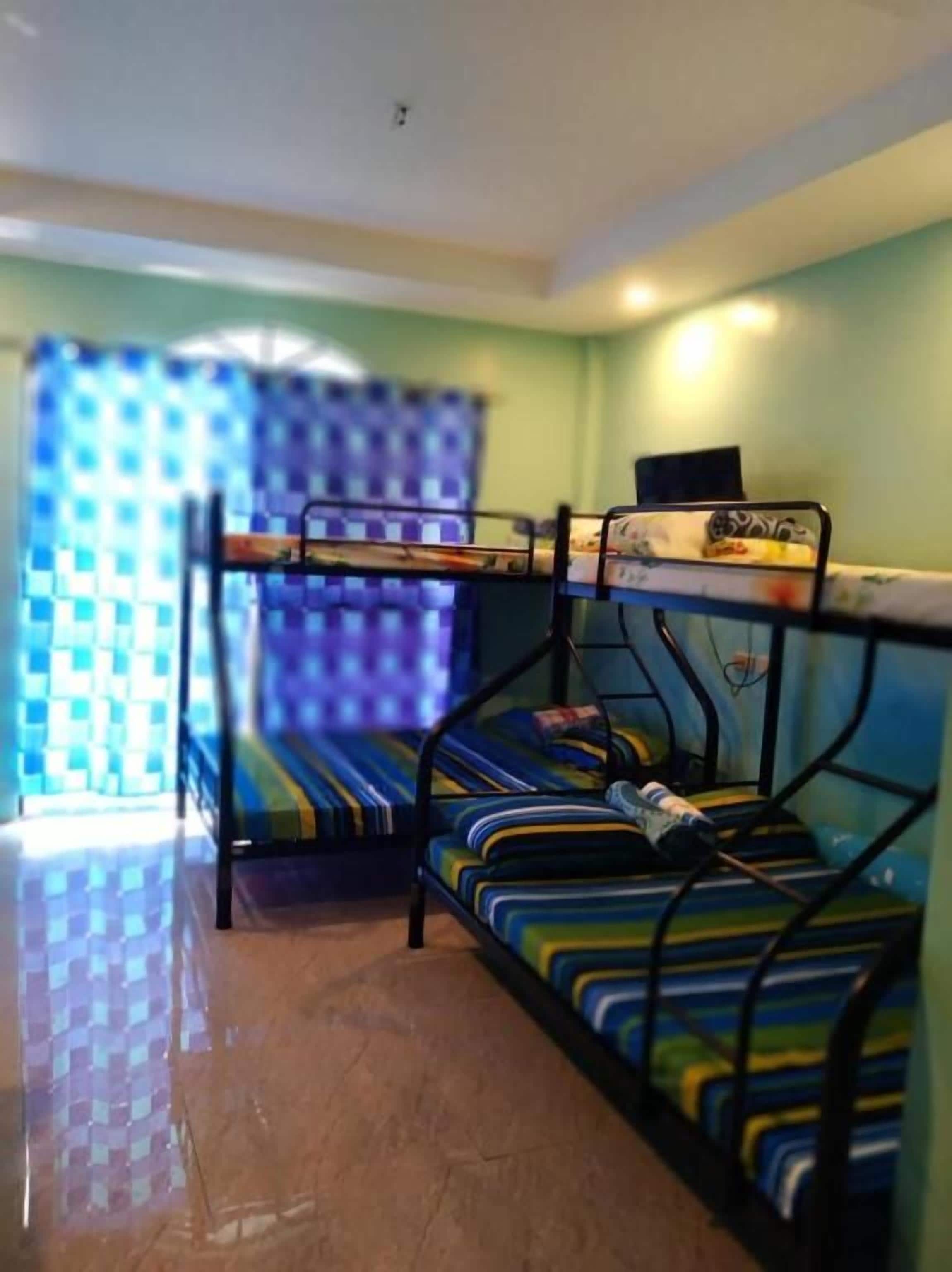 Une chambre avec des lits superposés, une fenêtre avec des rideaux bleus et un lit recouvert d’une couverture à rayures.