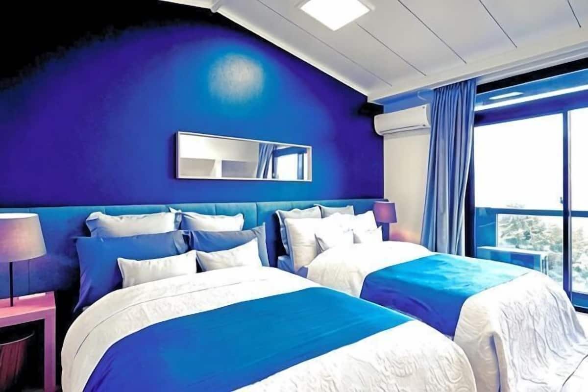 A hotel room with two beds, a large window, and a view of the city.