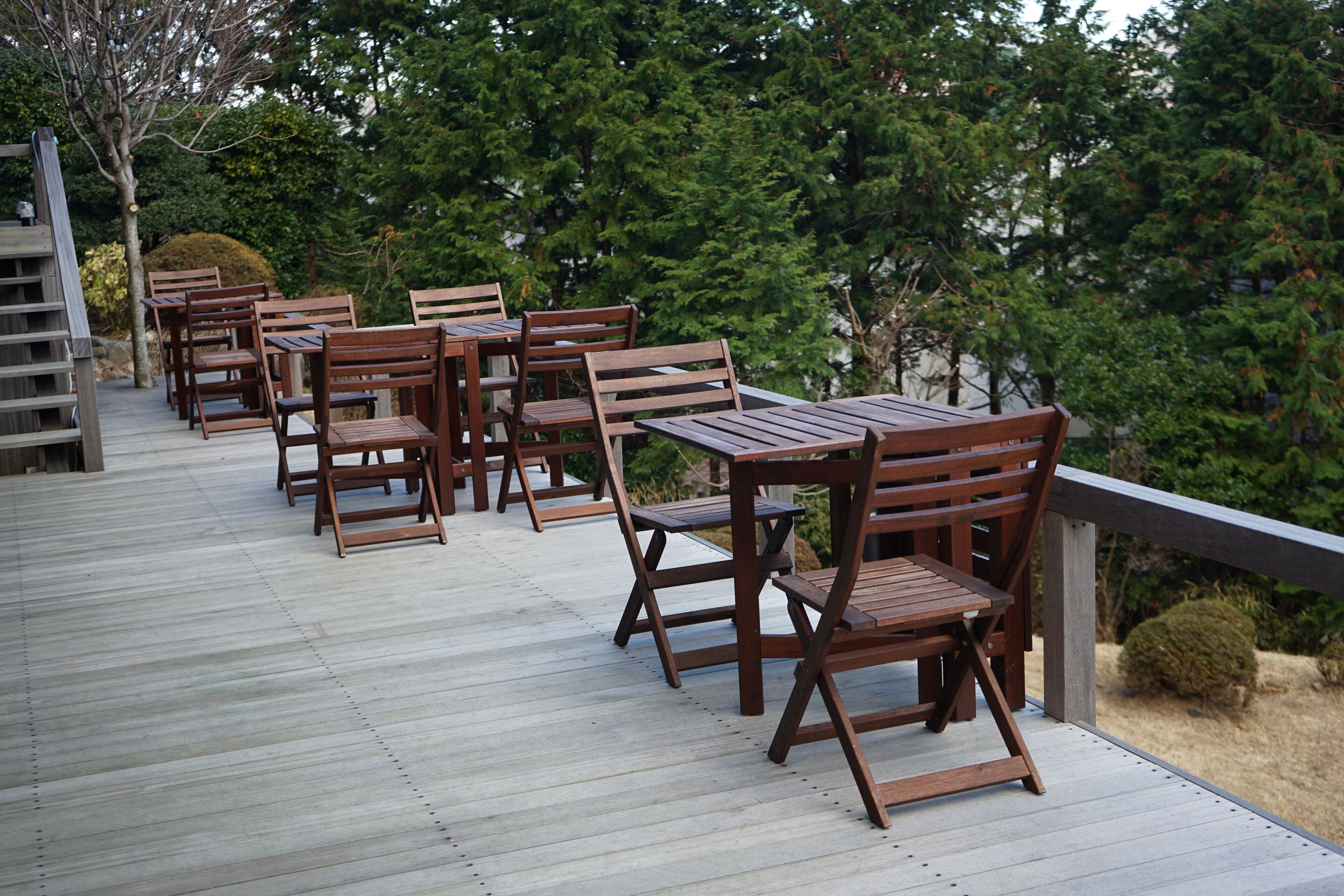 A wooden deck with tables and chairs, surrounded by trees.