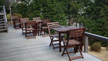 A wooden deck with tables and chairs, surrounded by trees.