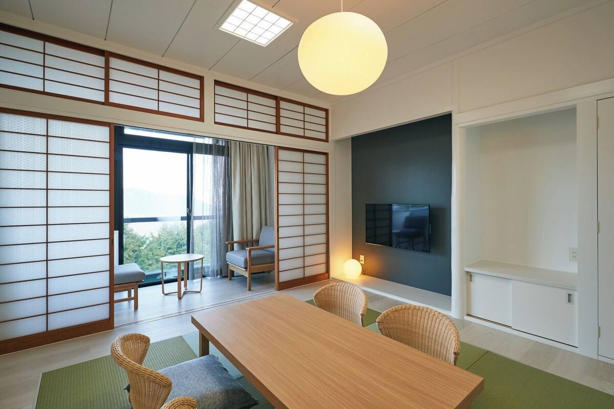A traditional Japanese-style room with tatami flooring, a low table, chairs, a TV, and a sliding door.
