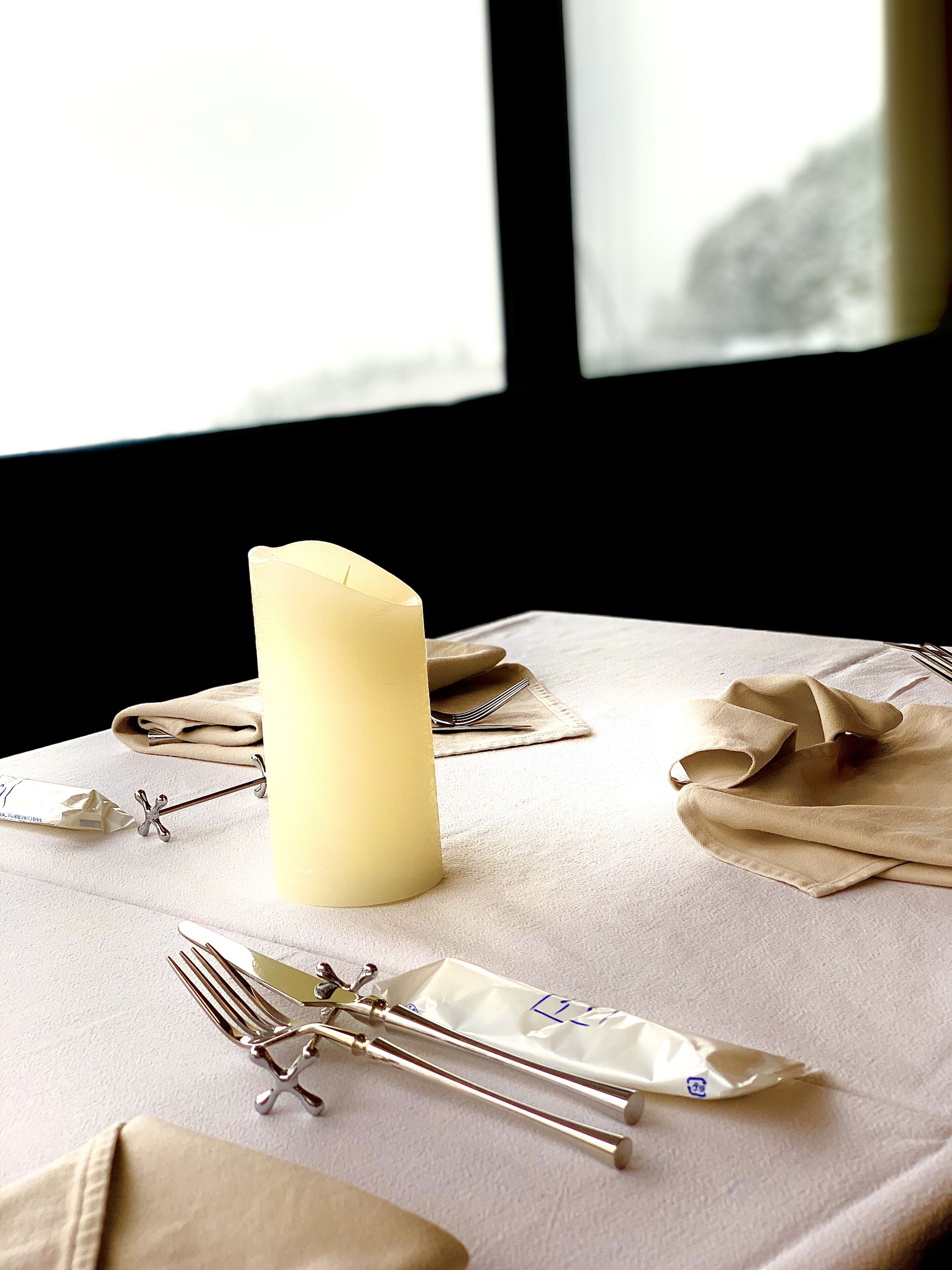Une table dressée avec une bougie, des serviettes pliées et des couverts.