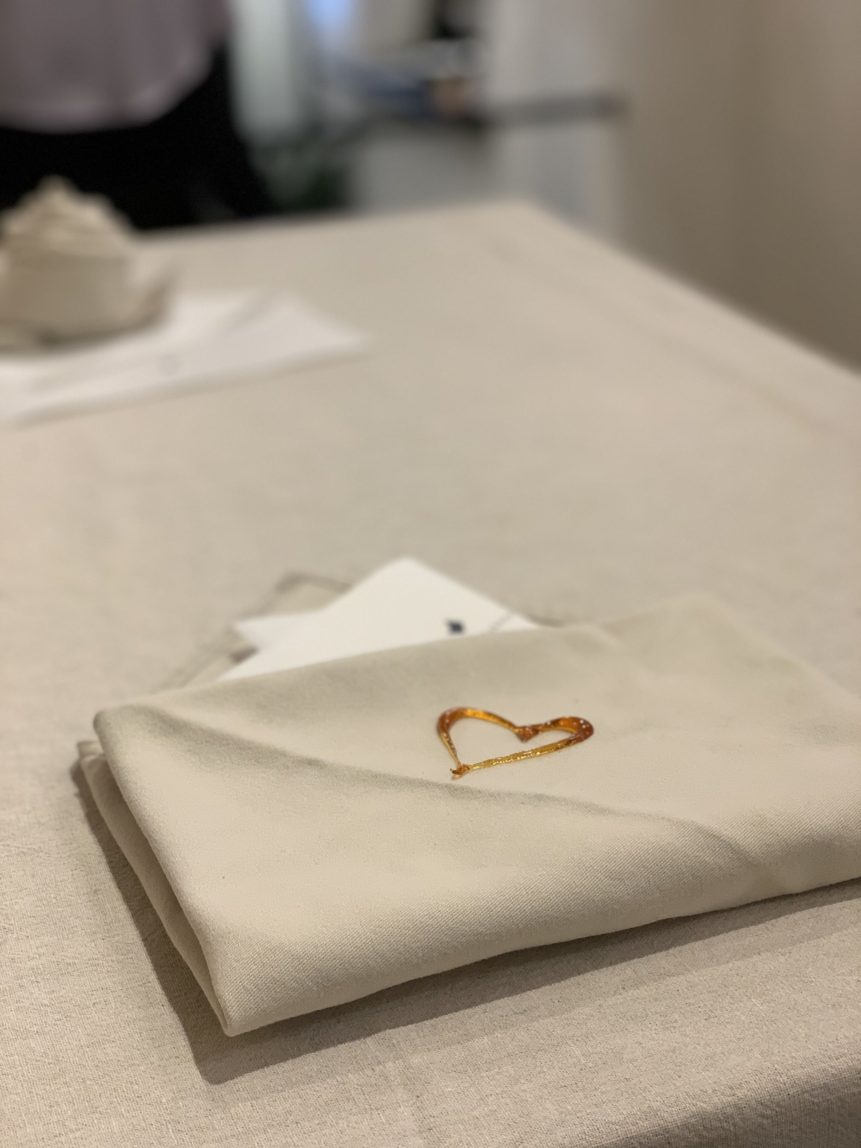 Un morceau de tissu beige, soigneusement plié, orné d’une broderie en forme de cœur, est posé sur une table.
