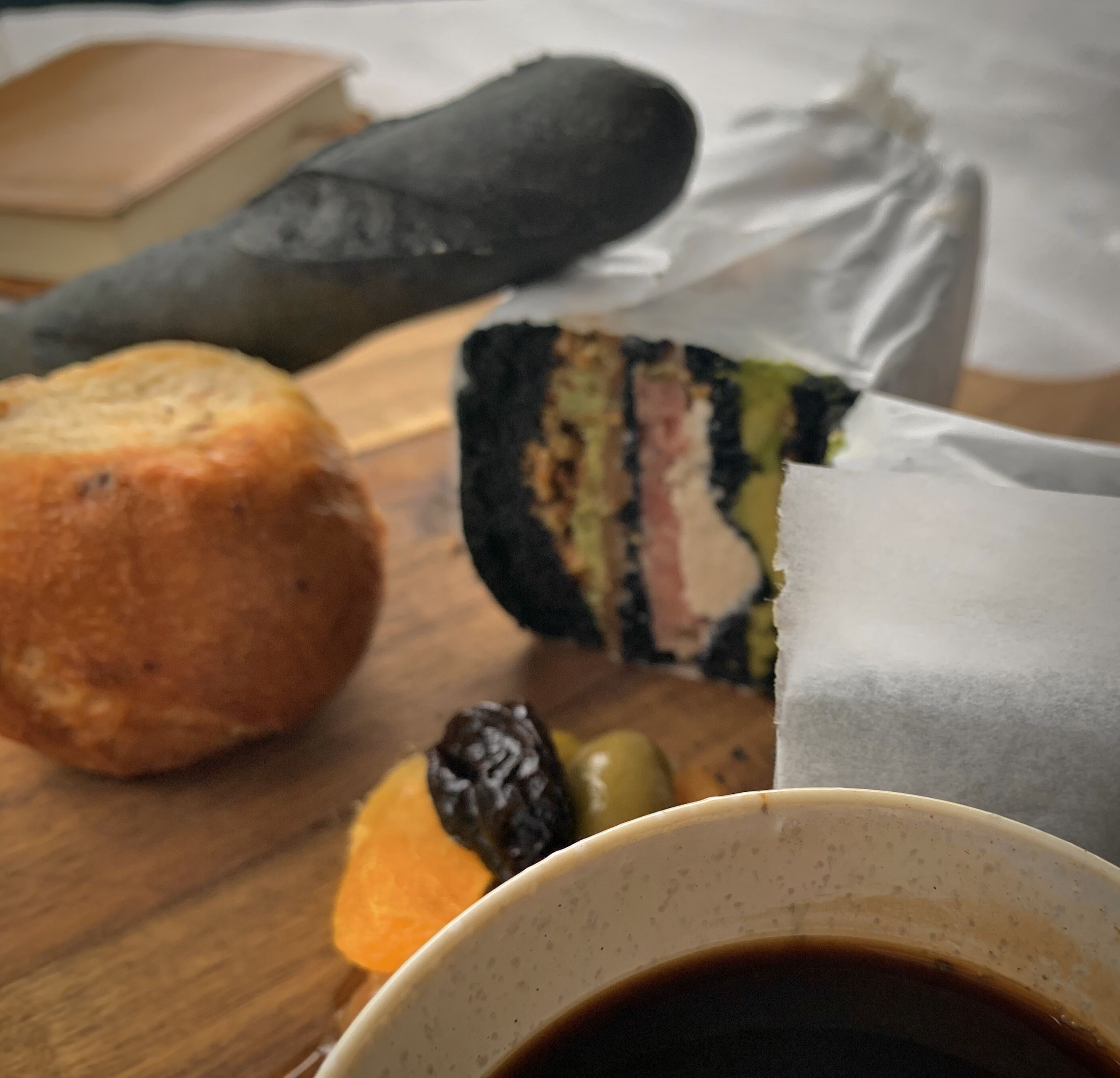 A wooden table with a pastry, a piece of cake, and a cup of coffee.