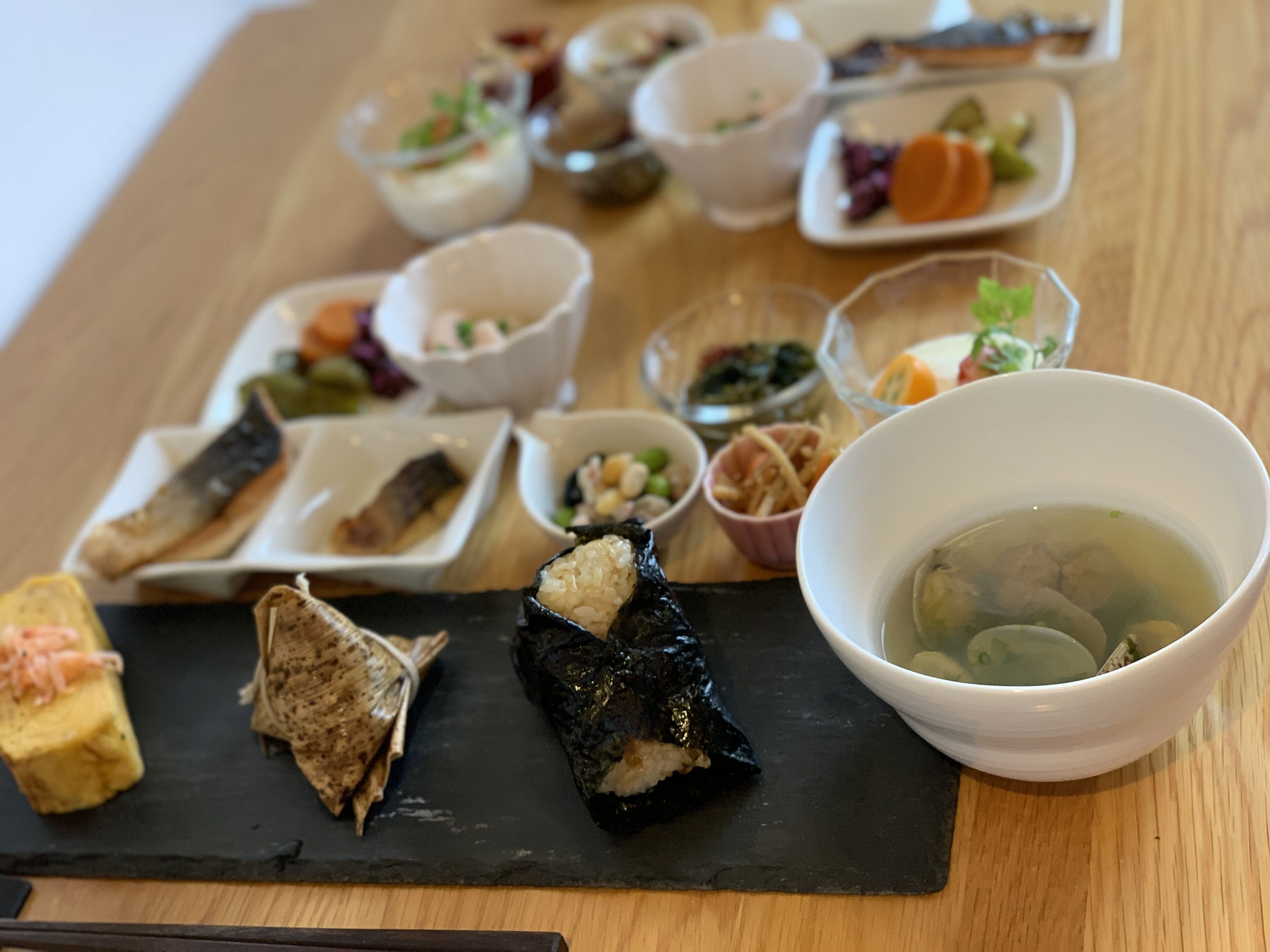 Verschiedene Gerichte auf einem Holztisch, darunter Sushi, Sashimi sowie kleine Schalen mit Suppe und eingelegtem Gemüse.