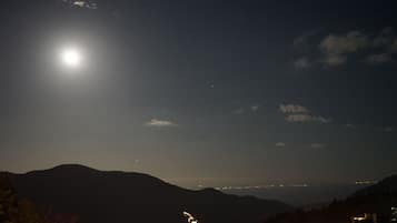 Vista nocturna de una zona montañosa con una luna brillante y luces de una ciudad a lo lejos.