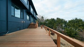 Eine Holzterrasse, die zu einem modernen Gebäude mit großen Fenstern und einem Holzgeländer führt.