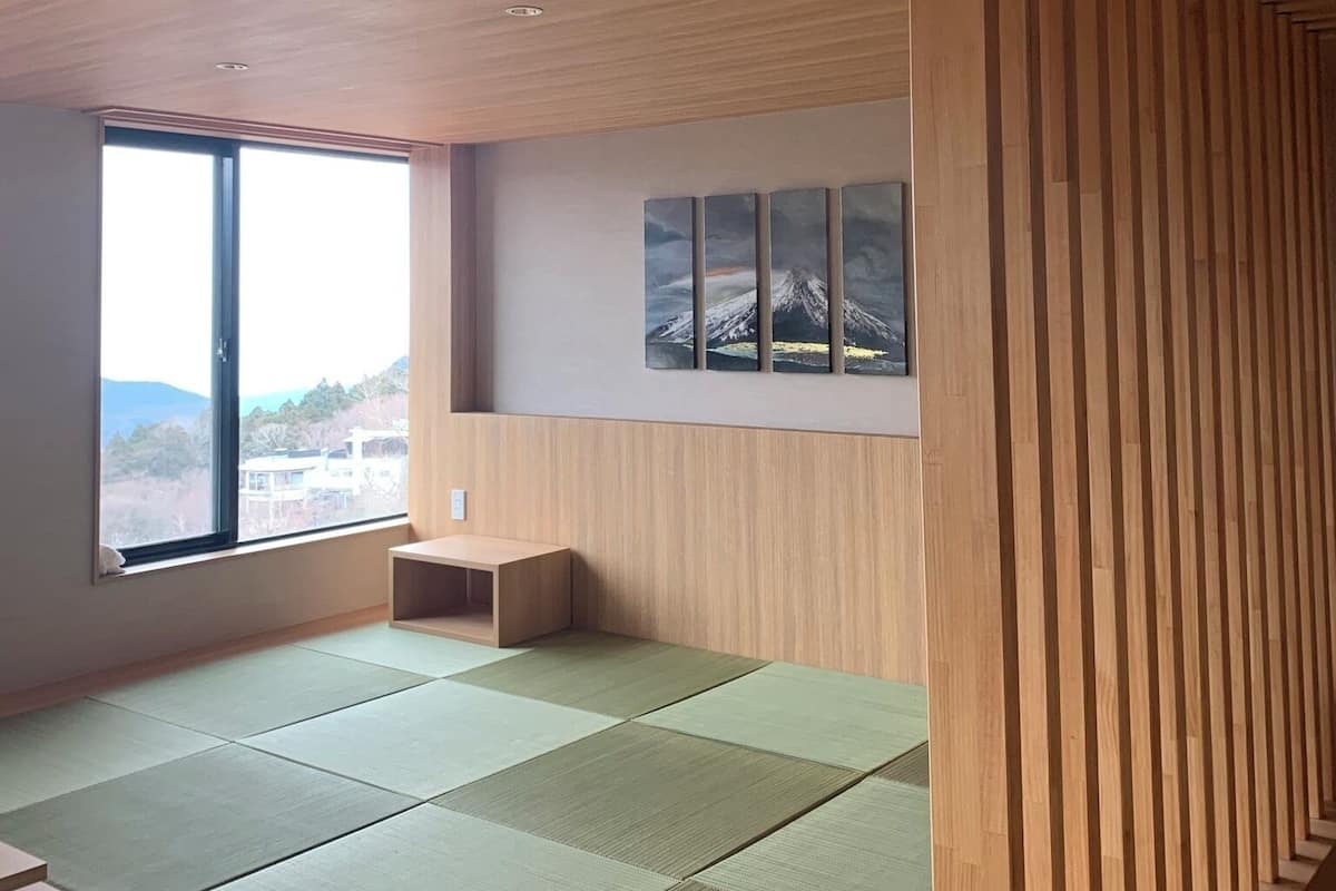 A room with tatami mats, a wooden partition, and a view of a mountain through a large window.