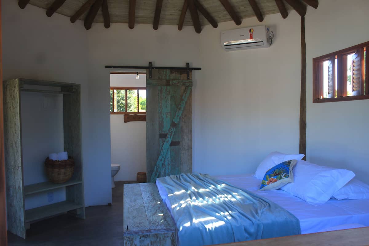 Quarto com cama, prateleira de madeira, janela com cortinas e ar-condicionado.