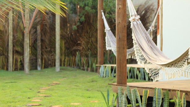 A hammock tied between wooden posts, a wooden deck, and a path with circular stepping stones. - Pousada Vila Cacau (Uruçuca)