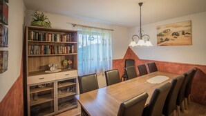 A dining area with a wooden table and chairs, a bookshelf, a window with curtains, and a painting on the wall. - Casa Melissa (Schönberg im Stubaital)