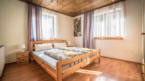 A wooden bed with a headboard, two bedside tables with lamps, and a window with curtains. - Casa Melissa (Schönberg im Stubaital)