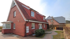 A red brick house with a sloped roof, a front porch, and a paved driveway. - Apartment Tietje, Germany (Sylt)
