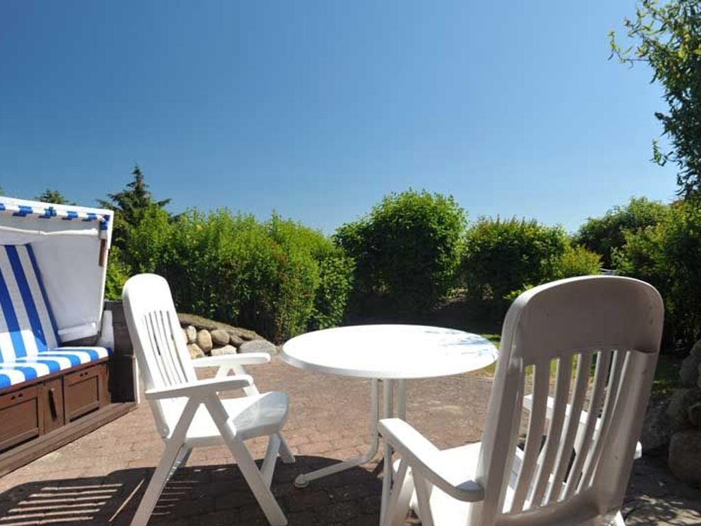 An outdoor seating area with a round table and two white chairs, a striped sofa, and a view of green trees and a clear sky.