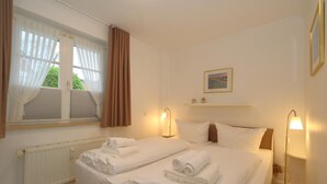 A hotel room with two beds, a radiator, a window with curtains, a picture on the wall, and bedside lamps. - Apartment Tietje, Germany (Sylt)