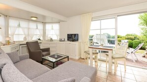 A spacious living area with a sofa, chairs, a coffee table, a TV, and a dining table. - Apartment Tietje, Germany (Sylt)