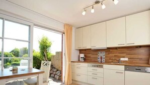 A modern kitchen with white cabinets, a wooden countertop, and a dining area with a table and chairs. - Apartment Tietje, Germany (Sylt)