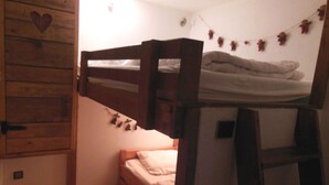 Ein kleiner, gemütlicher Raum mit einem Etagenbett, einem Holzschrank mit Herzmotiv und einem Wandregal mit Dekoration.