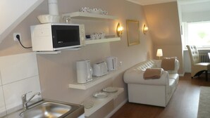 A compact kitchen with a microwave, toaster, and kettle, a white sofa, and a dining area with a table and chairs. - Teewelkenhüs sun apartment (Sylt)