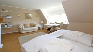 A bedroom with a bed, a desk, a chair, a sofa, and a window. - Teewelkenhüs sun apartment (Sylt)