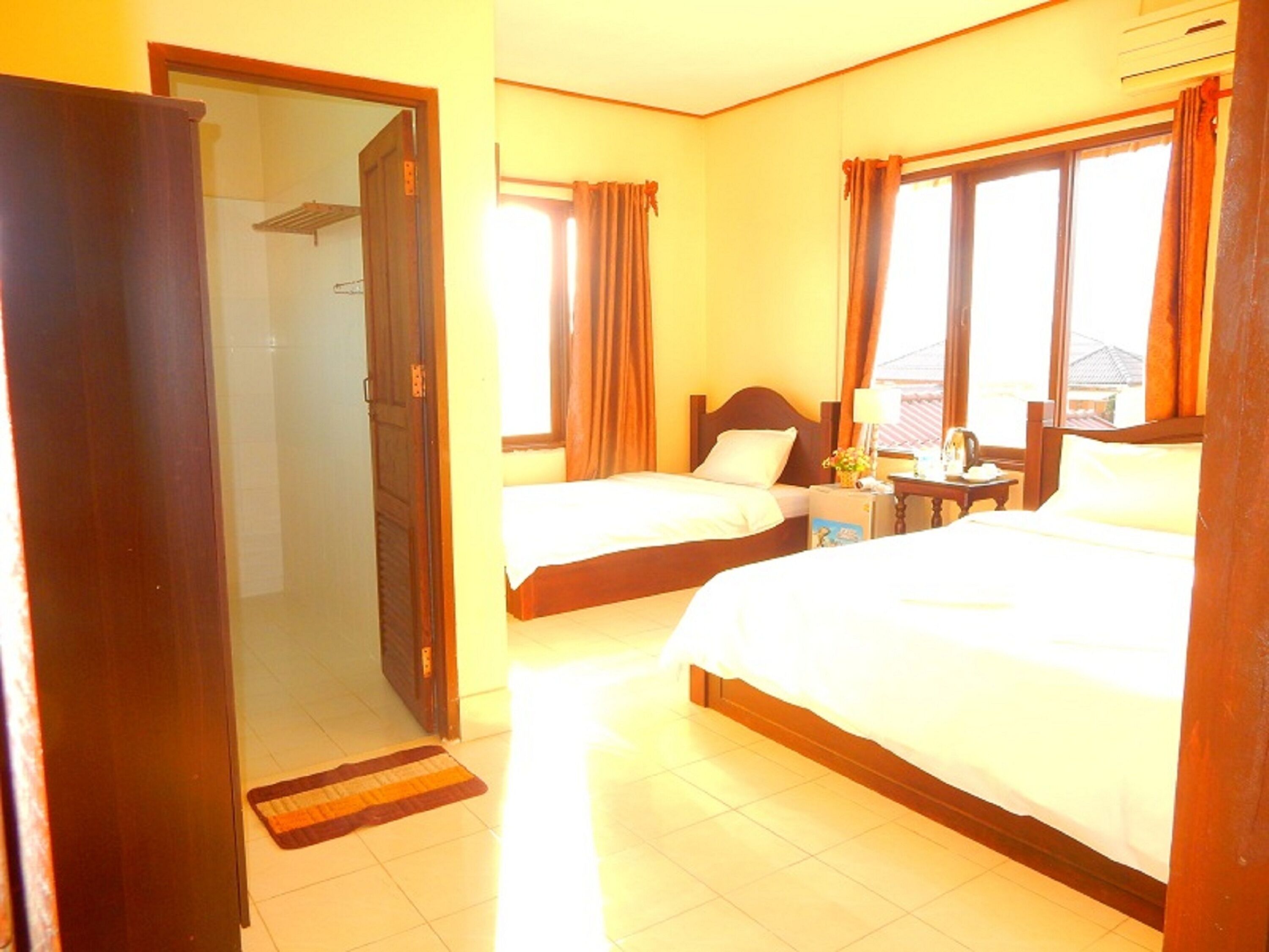Habitación de hotel con dos camas, un armario, una mesita con lámpara y un ventanal con cortinas.