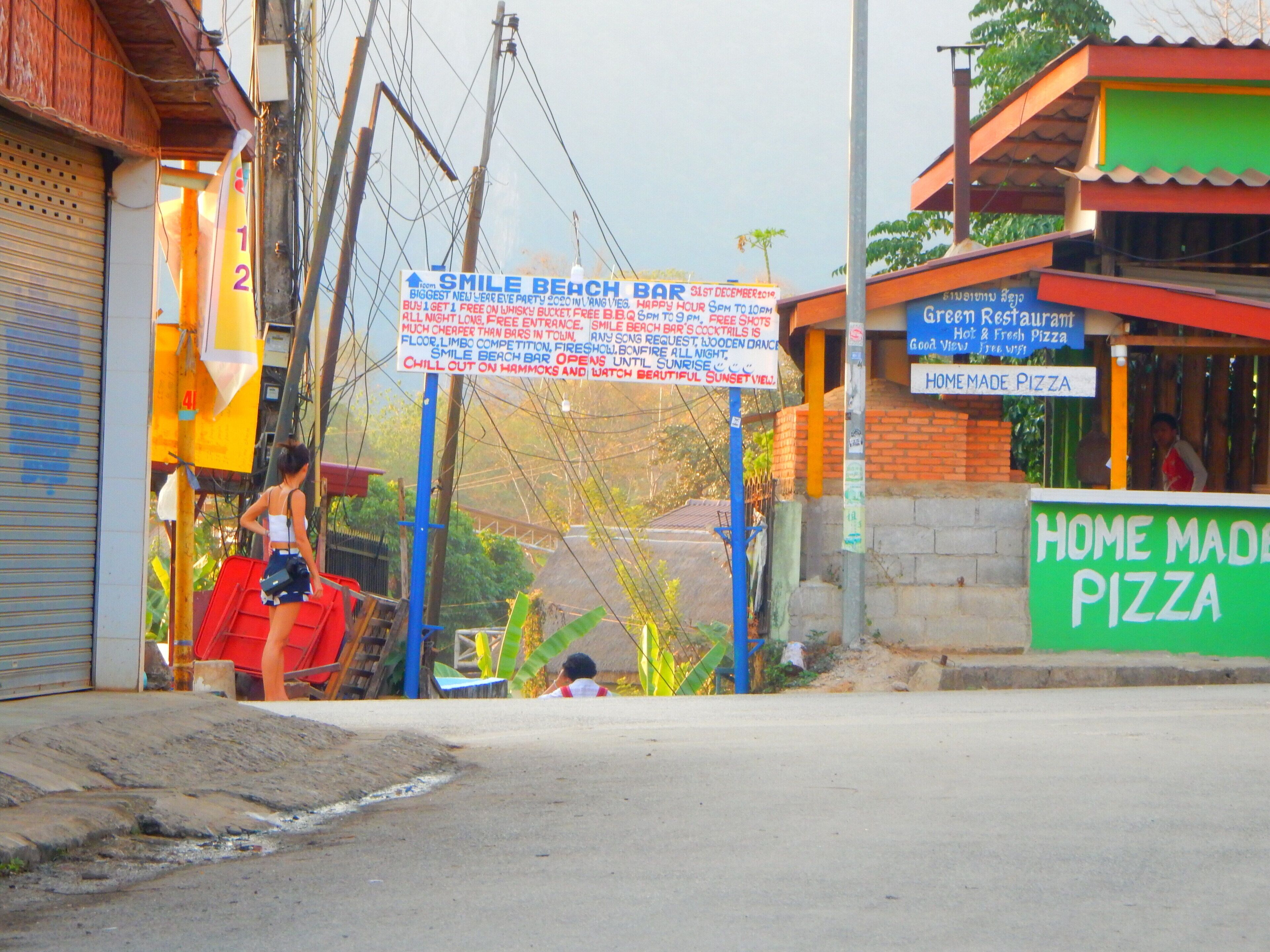 A street view with a sign for Smile Beach Bar and a Home Made Pizza restaurant.