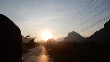 A road with a sunset in the distance, power lines, and mountains.