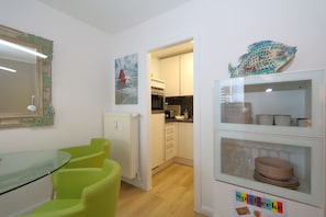 A modern kitchen with white cabinets, a refrigerator, and a dining area with a glass table and green chairs.