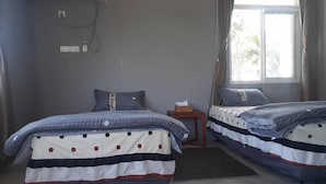Une chambre d’hôtel avec deux lits, une petite table, un appareil de climatisation et une fenêtre avec des rideaux.