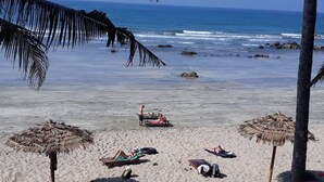 Une plage bordée de palmiers, avec des parasols en feuilles de palmier et des gens qui se détendent sur le sable.