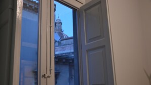 Puerta abierta que da a un balcón con vista a un edificio con cúpula y una cerca.