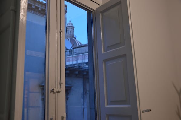 An open door leading to a balcony with a view of a building with a dome and a fence.