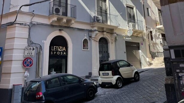 Un edificio con un letrero que dice "LETIZIA Sposa" y un cartel de no estacionamiento. Hay coches aparcados en la calle.