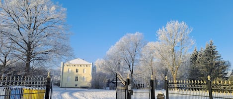 A snow-covered pathway leading to a building with a white facade and a metal gate.