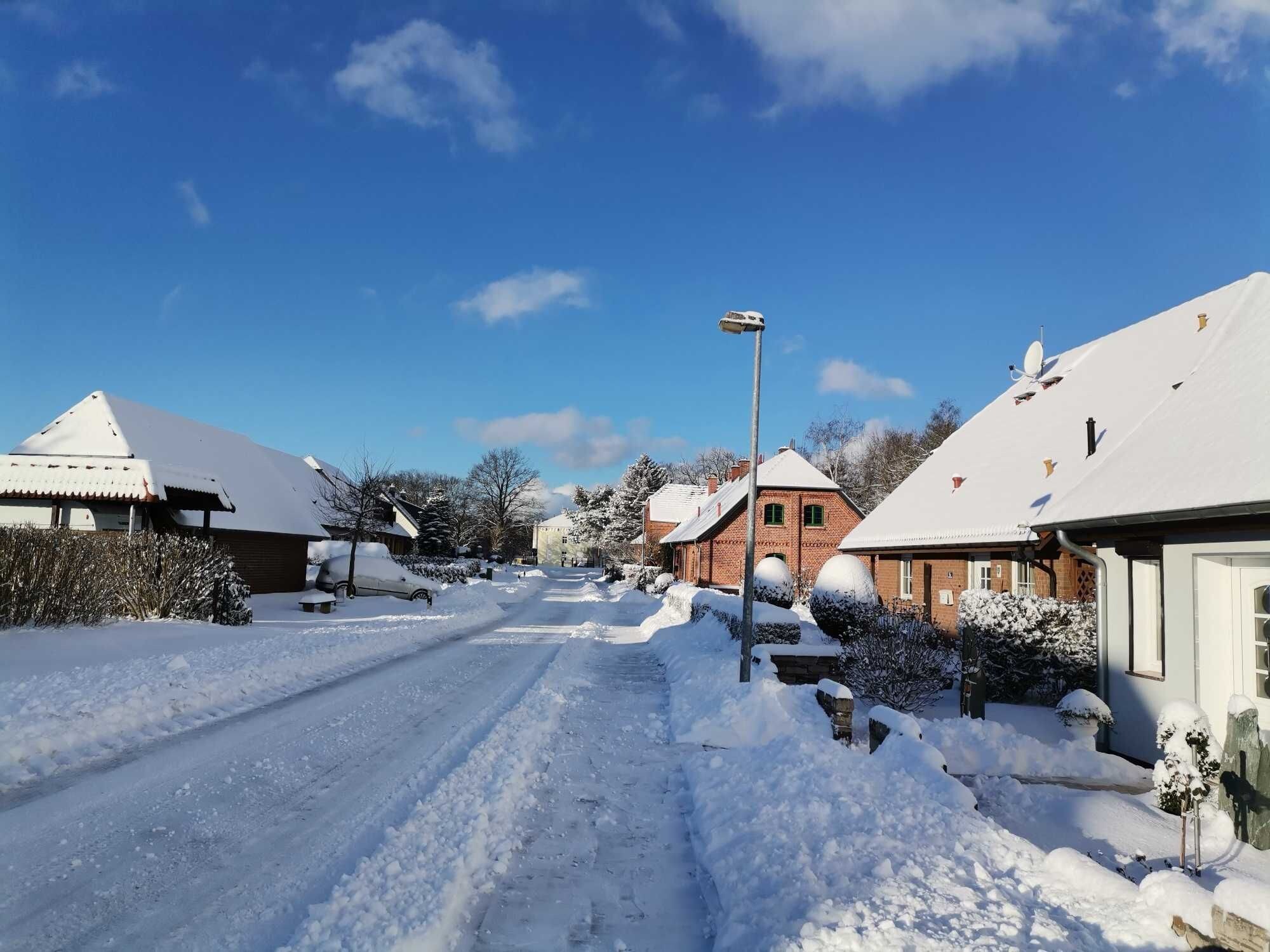 A snow-covered street with houses, a street lamp, and a clear blue sky.