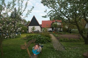 En have med en bænk, en lille hvid bygning og et hus med rødt tag.