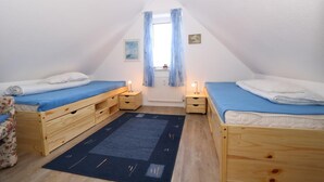 A small, triangular attic bedroom with two wooden beds, a dark rug, and a window with curtains. - Vacation apartment Reinhardt (Sylt-Ost)
