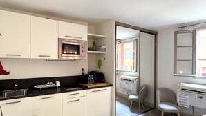 Eine kompakte Küche mit weißen Schränken, einer eingebauten Mikrowelle und einer Glastür, die auf einen Balkon mit einem Stuhl und einem Heizkörper führt.