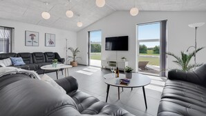 A modern living room with a sofa, coffee table, and TV. There are large windows and a view of the outdoors. - Lovely home in Jerup with sauna (Jerup)