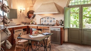 A kitchen with a stone arch, a dining table with chairs, a stove, and a view of greenery through a door. - Beautiful private villa for 16 guests with A/C, WIFI, private pool, TV, patio and panoramic view (Montalcino)