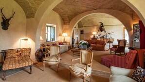 A spacious living room with a high arched ceiling, rustic brick walls, and a fireplace. There are multiple seating areas with various chairs and sofas. - Beautiful private villa for 16 guests with A/C, WIFI, private pool, TV, patio and panoramic view (Montalcino)
