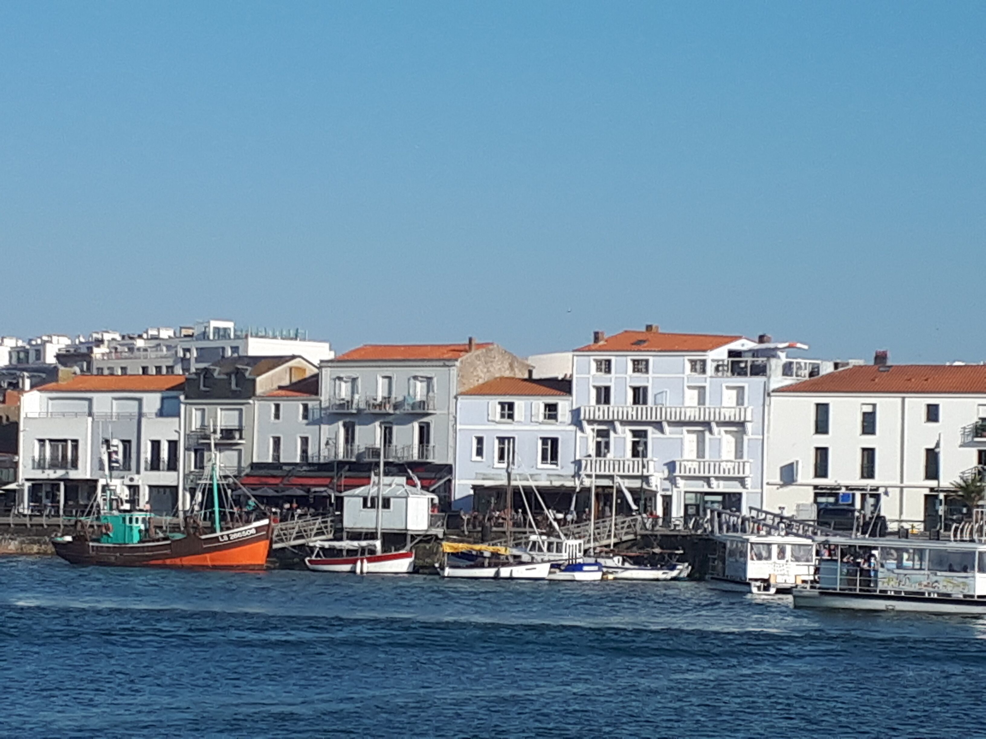 Un port où plusieurs bateaux sont amarrés et où se trouvent des bâtiments le long de la rive.