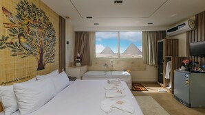 A hotel room with a bed, a bathtub, a television, and a view of the pyramids. - Sun Pyramids View Inn (Giza)