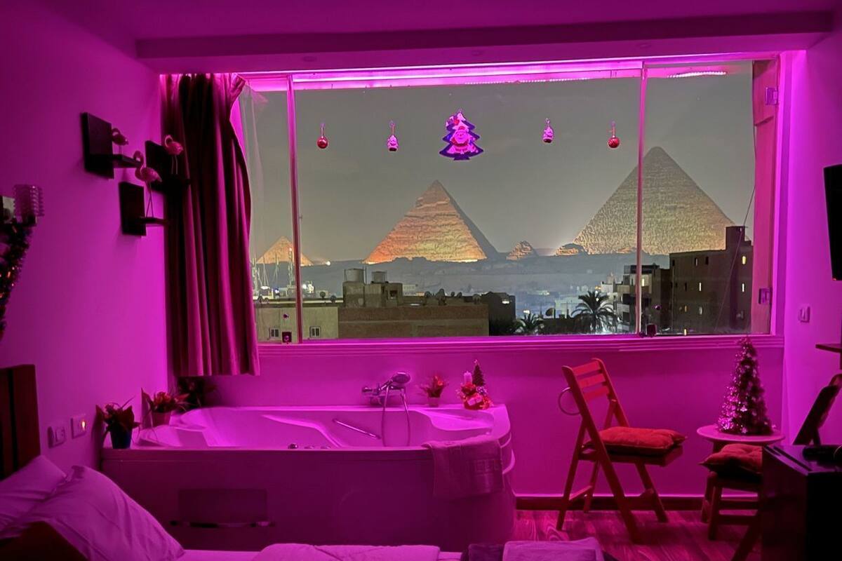 Un dormitorio con un ventanal grande, una cama, una silla y una mesita.