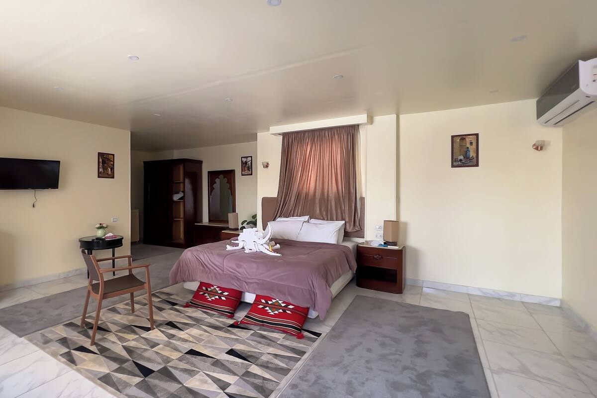 Habitación de hotel con cama, mesita de noche, televisor, armario y un pequeño escritorio con silla.
