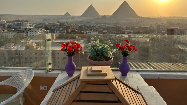 A balcony with a view of the pyramids, a table with wooden slats, and two purple vases with red flowers. - Sun Pyramids View Inn (Giza)
