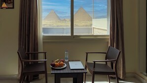 A room with a view of the pyramids, a table with fruit and a laptop, and two chairs. - Sun Pyramids View Inn (Giza)