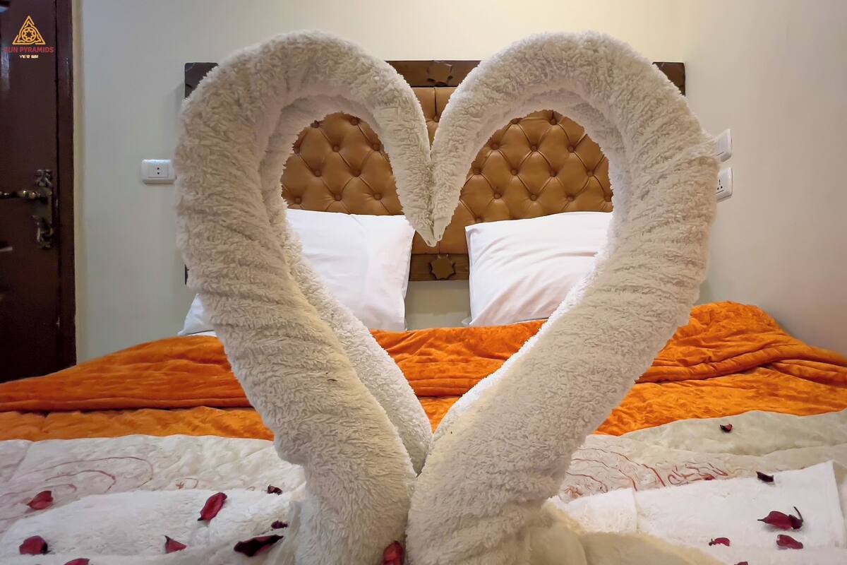 Una cama con un arreglo de almohadones blancos y esponjosos en forma de corazón y una manta naranja.