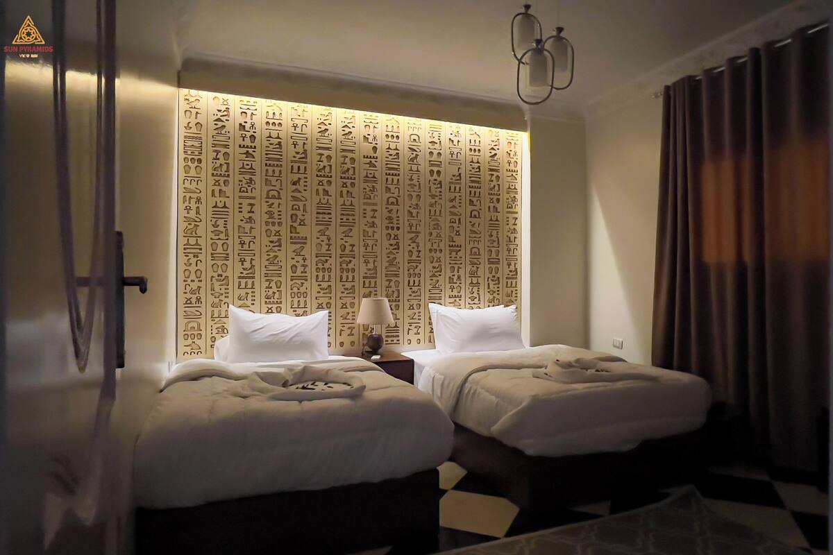 Habitación de hotel con dos camas, un cabecero estampado, una lámpara y un suelo a cuadros.